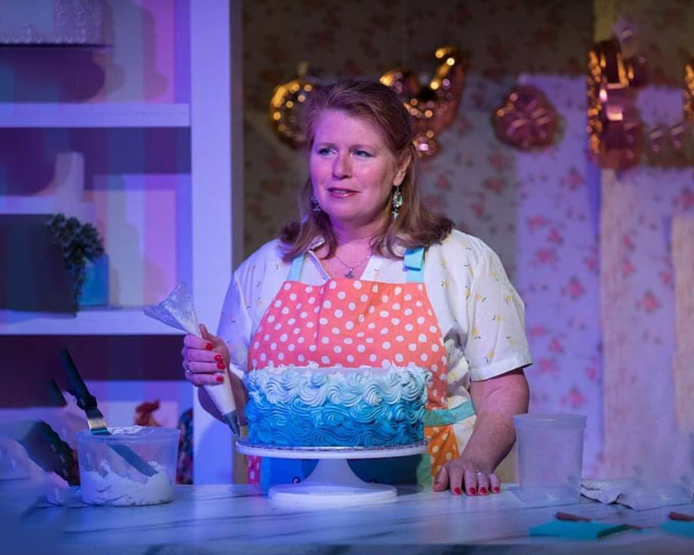 An actress adding frosting to a cake while looking into the distance