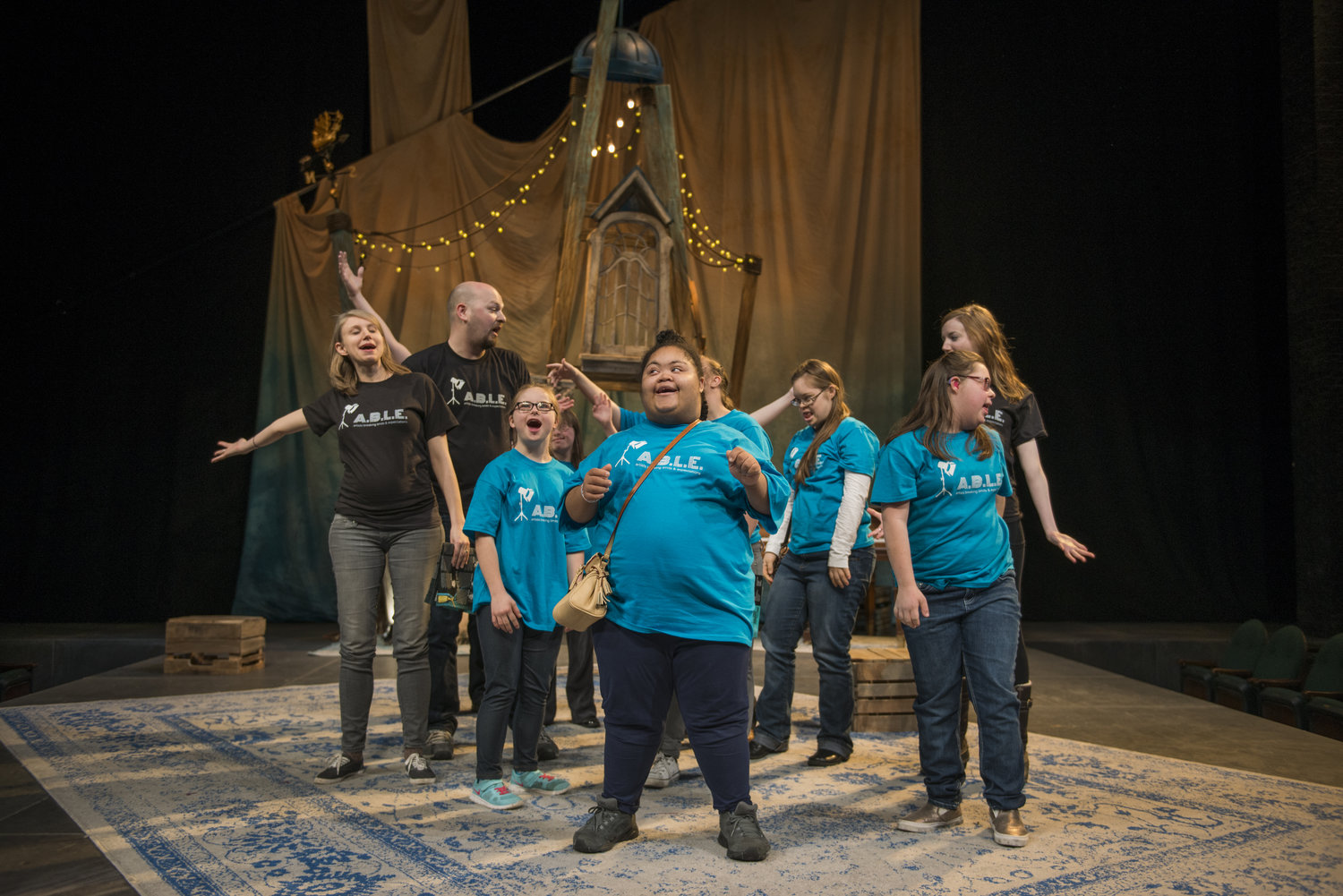 A cast of actors on stage looking in various directions